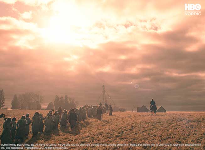 En rekke med arbeidskvinner, vandrende i et prærielandskap. Til høyre sees en mann til hest, muligens en vakt. Dramatisk, gyldent lys.