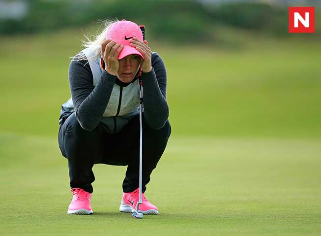 Golfspilleren Suzann Pettersen, sittende på huk på en golfbane med begge hendene på hodet, dypt konsentrert eller fortvilet.