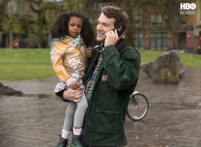 Voksen mann prater i mobiltelefon mens han bærer datteren sin i den andre armen.